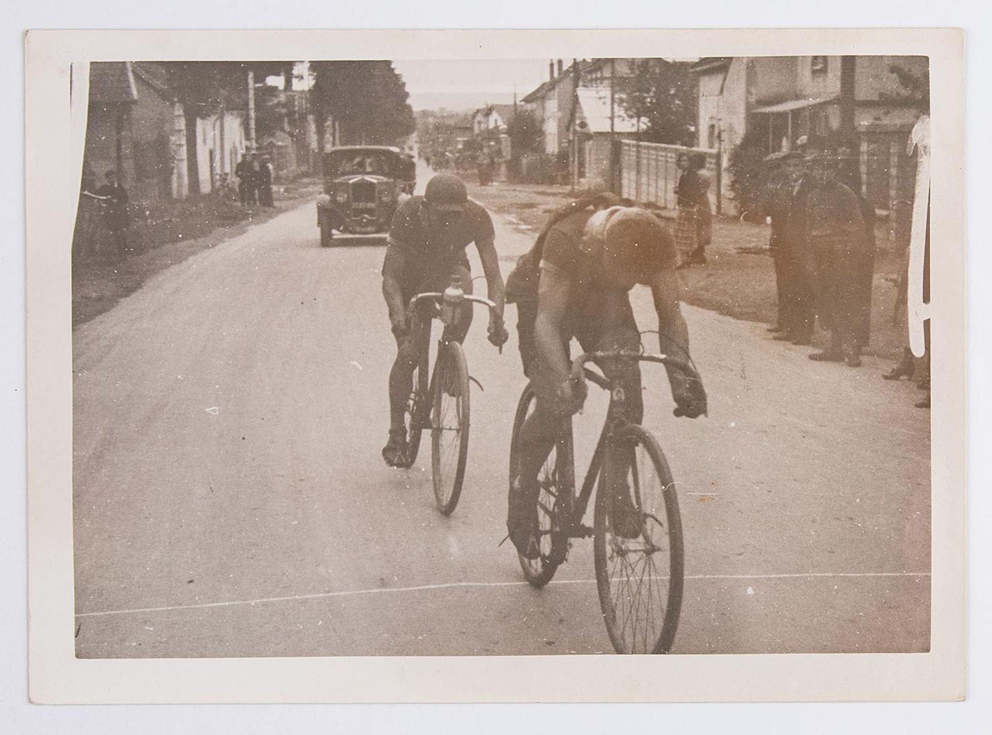 Deux cyclistes traversant un village. Course et lieu à identifier.