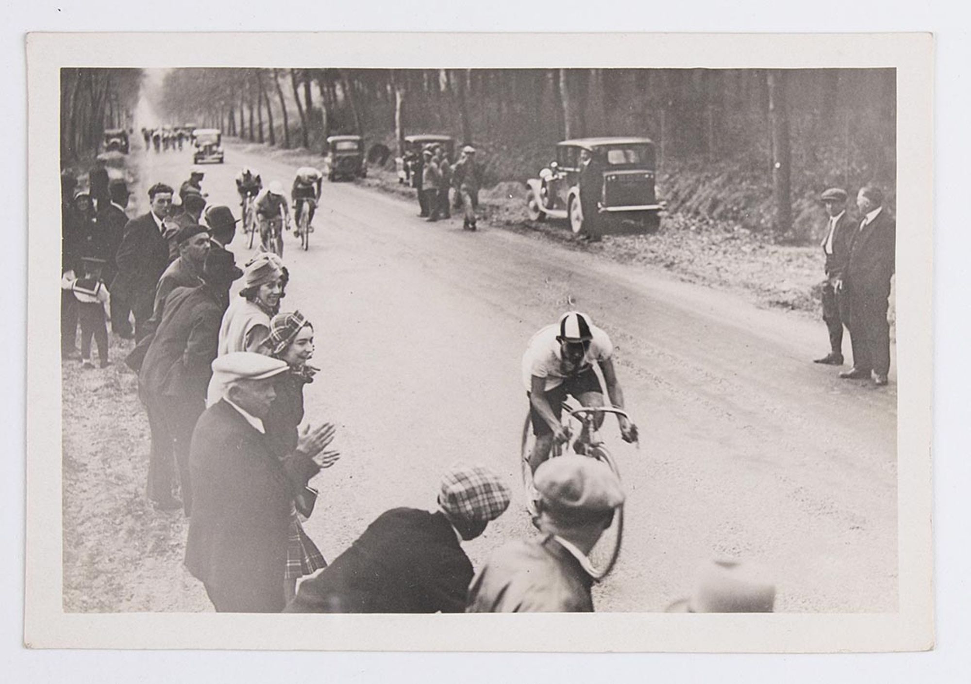 1933. Un groupe de cyclistes traverse une forêt au milieu des spectateurs. Course et lieu à identifier.