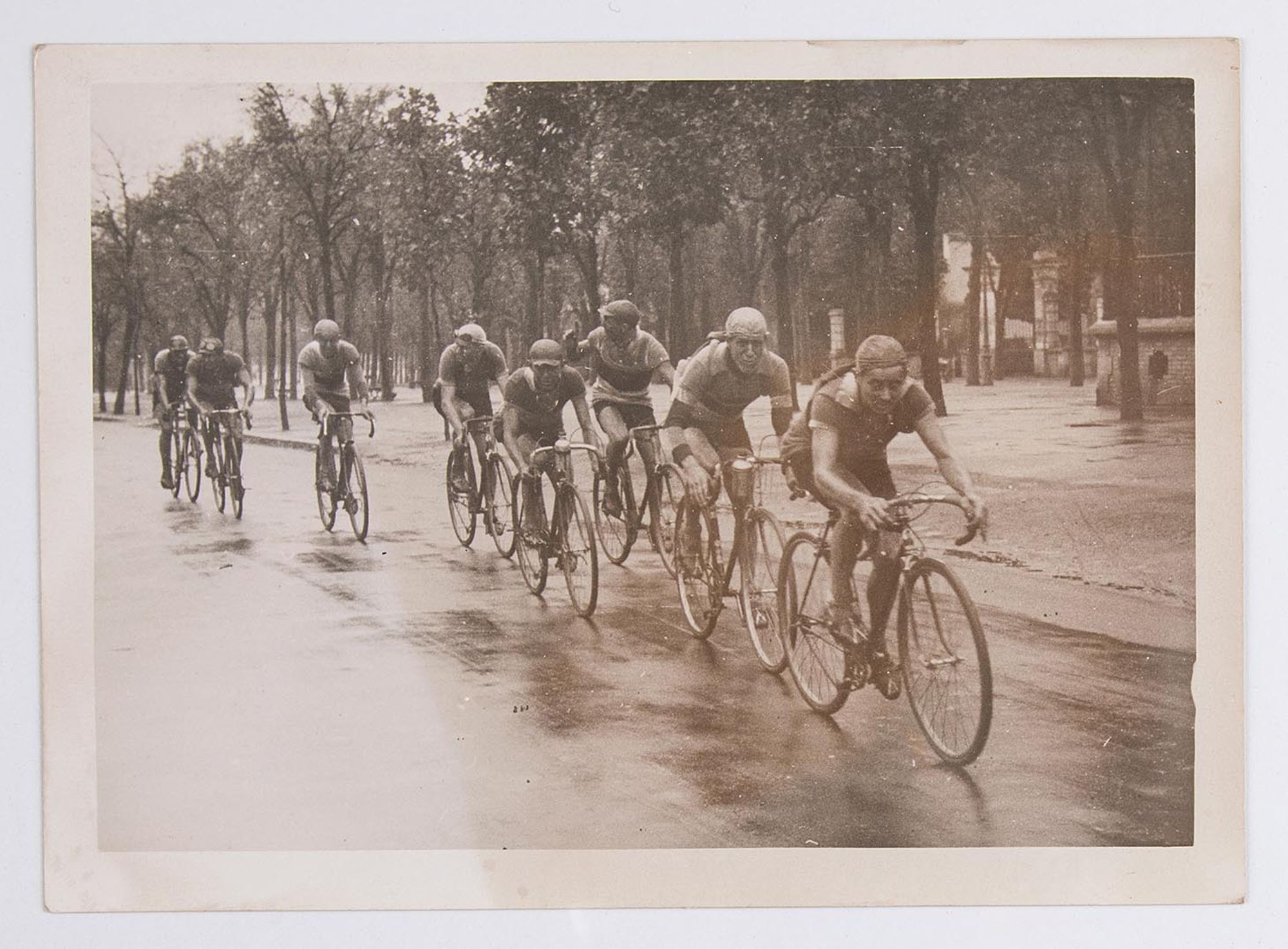Un groupe de coureurs cyclistes sous la pluie. Lieu non identifié.