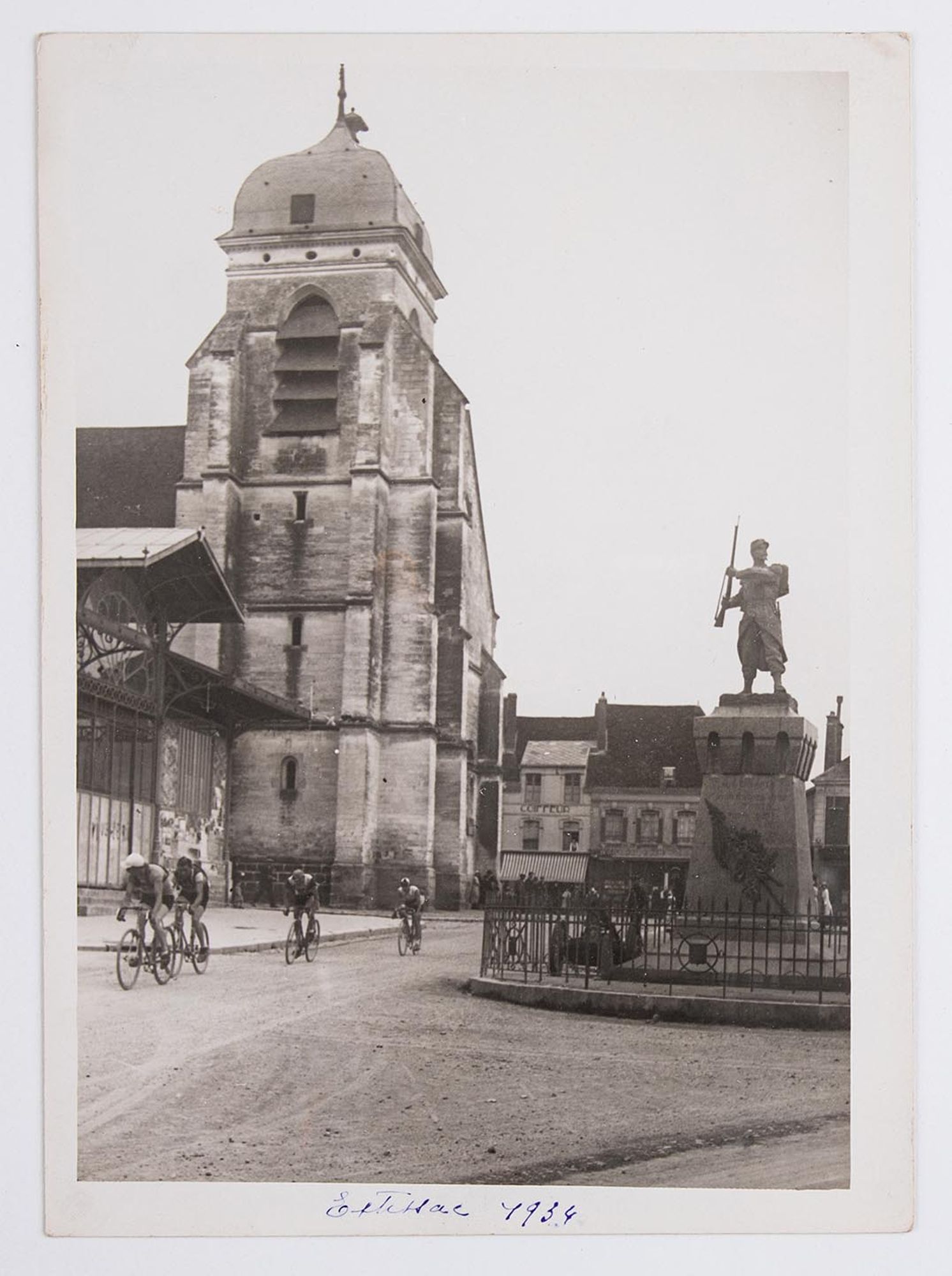 1934. Passage d'un groupe de coureurs cyclistes devant l'église, le marché et le monument aux morts d'Aix-en-Othe.