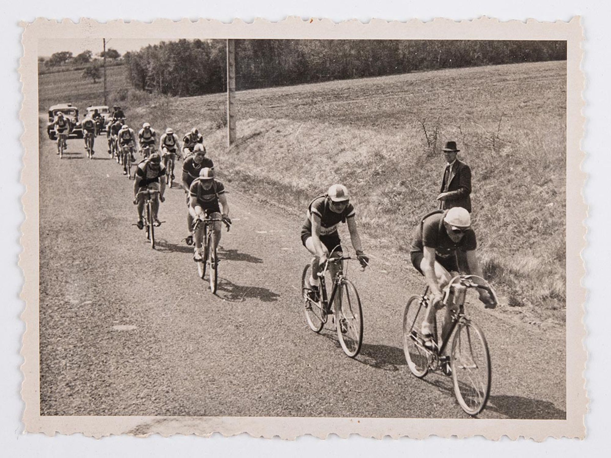 6349. Première vue d'une série de six tirages photographiques représentant une course non identifiée. Deux coureurs en tête du peloton, dans la campagne. Lieu à identifier.