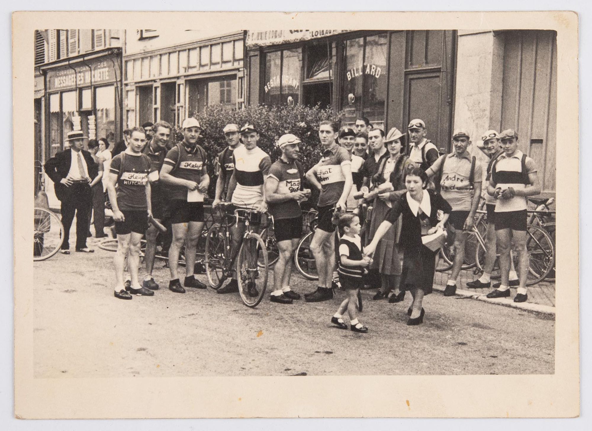 Un groupe de coureurs cyclistes, dont J. Krubs, au milieu, posent dans une rue, devant des commerces. Lieu à identifier.